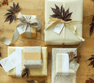Four wrapped gifts on a wooden surface with autumn leaves.