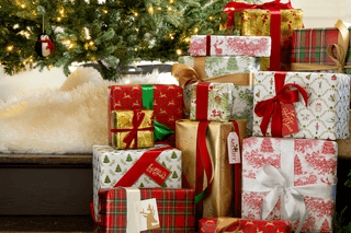 Stack of Christmas presents under a decorated tree with lights.