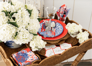 Table setting with white flowers, red and blue plates, and napkins on a wicker tray.